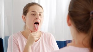 Portrait of young woman checking her teeth and tongue for plaque at mirror in bathroom