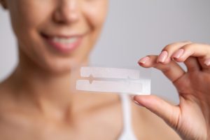 Teeth whitening, beautiful smiling woman holding a whitening strip.