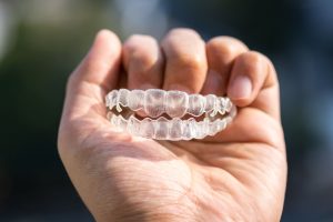 Hand holding a set of upper and lower clear aligner trays outdoors in sunlight