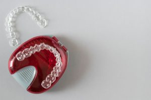 Two clear aligner trays, one resting on a red plastic storage case, on a gray background