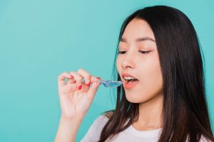 Young woman about to place a blue removable orthodontic retainer with a wire into her mouth against a teal background